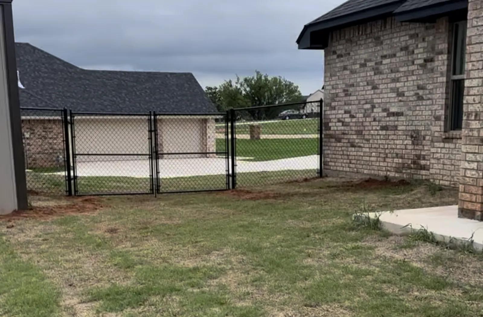 Black chain link fence with a double drive gate installed beside a brick home in the Oklahoma City metro