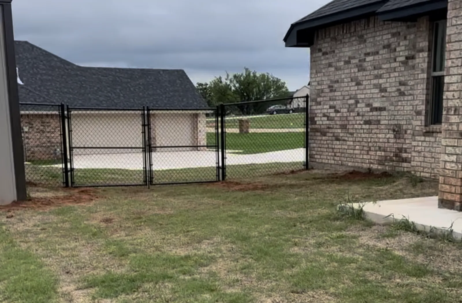 Black chain link fence with a double drive gate installed beside a brick home in the Oklahoma City metro