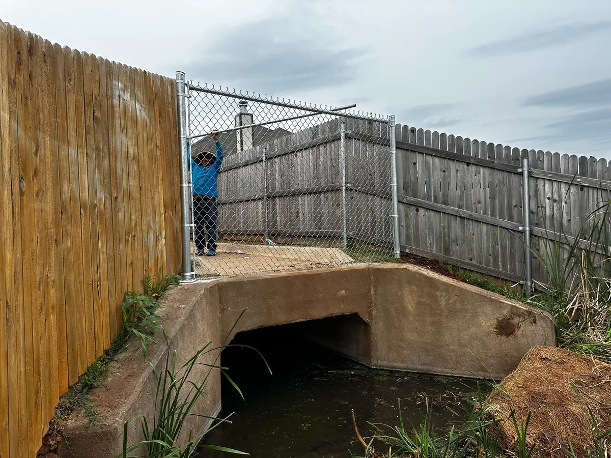Galvanized chain link fence spanning a concrete drainage culvert between wood privacy fences in Oklahoma City